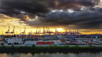 A sleek aerial view of Rotterdam's bustling port at dusk, highlighting cranes and container ships under moody skies.