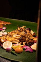 A platter of assorted grilled seafood placed on a large green banana leaf. It is garnished with lemon slices, red onions, green chili peppers, and a whole egg yolk. The seafood appears to be seasoned and cooked with a slightly charred look.