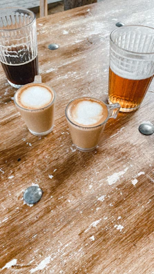 A rustic wooden table with freshly brewed coffee and a glass of craft beer side by side.