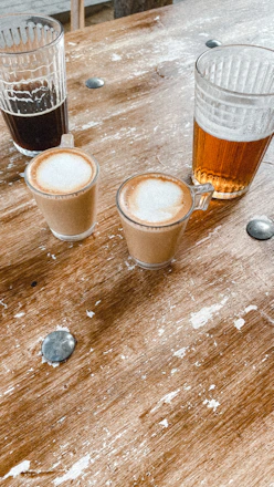 A cozy tasting setup with glasses of craft beer and cups of Colombian specialty coffee on a wooden table.