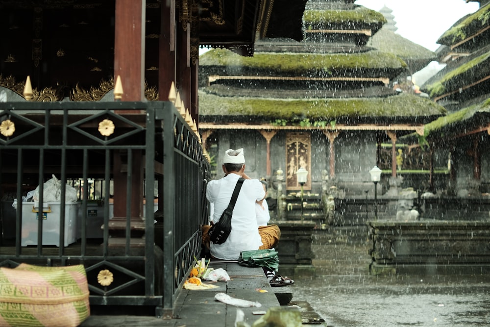 a man sitting on a ledge in the rain