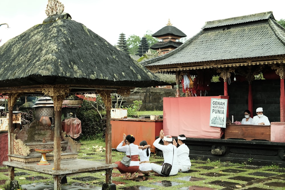 a group of people sitting on the ground in front of a gazebo