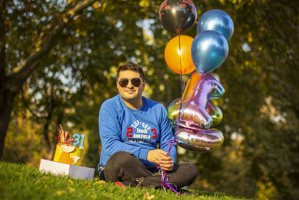 a man sitting in the grass with a bunch of balloons