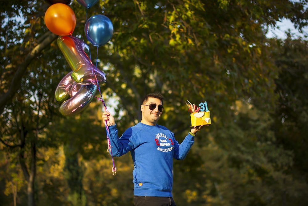 um homem em uma camisa azul segurando uma caixa e balões