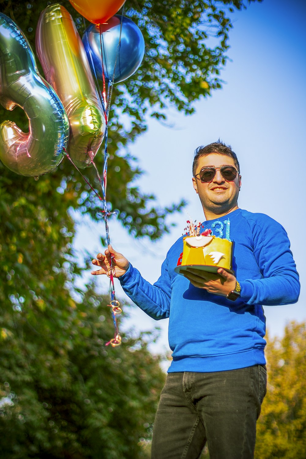 a man in a blue shirt holding a box and balloons