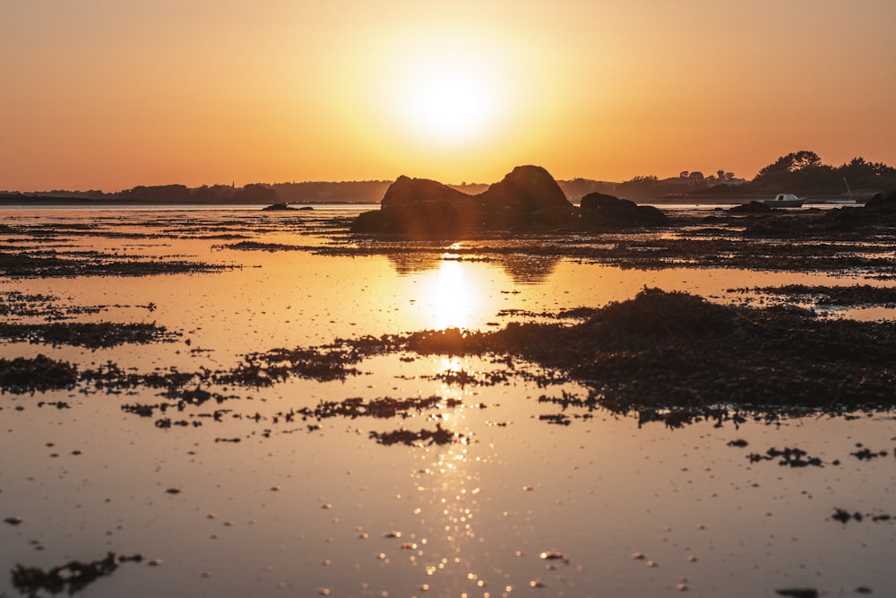 the sun is setting over the water and rocks