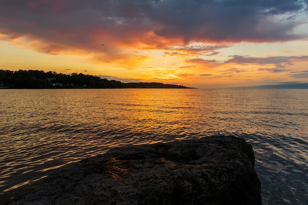 a sunset over a body of water with a large rock in the foreground