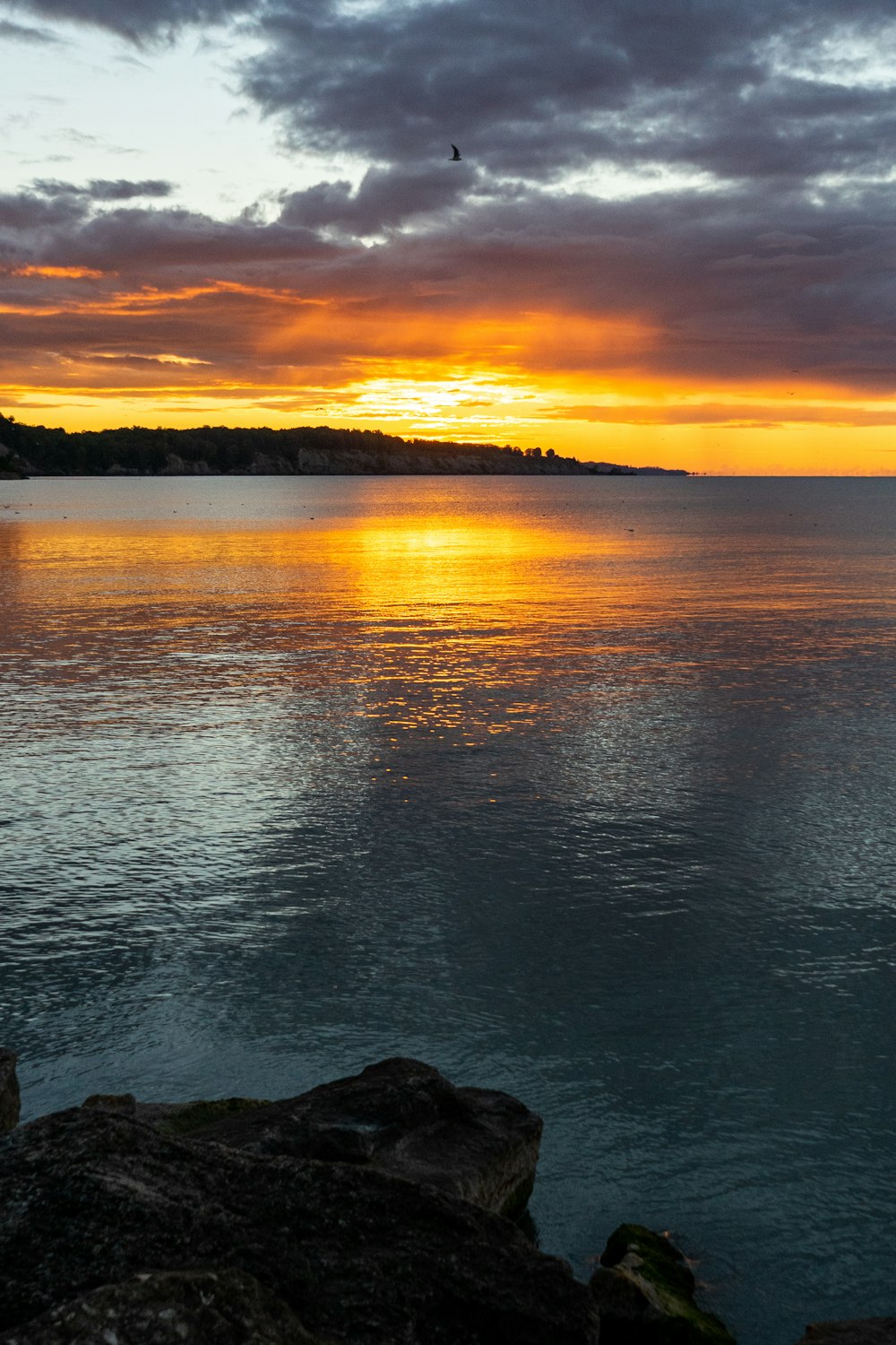 a sunset over a body of water with rocks in the foreground