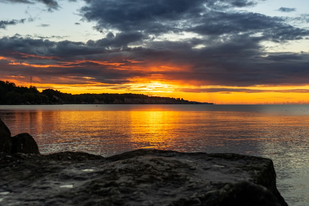 a sunset over a body of water with rocks in the foreground