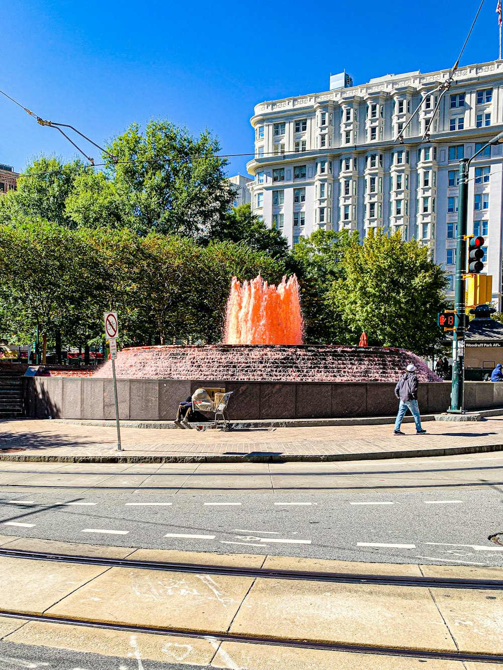 a man walking across a street next to a fountain