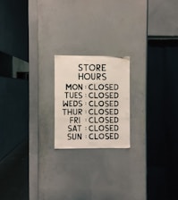 A sign posted on a wall listing the store hours, indicating the store is closed every day of the week.