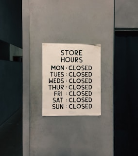 A sign posted on a wall listing the store hours, indicating the store is closed every day of the week.