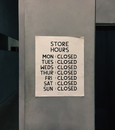 A sign posted on a wall listing the store hours, indicating the store is closed every day of the week.