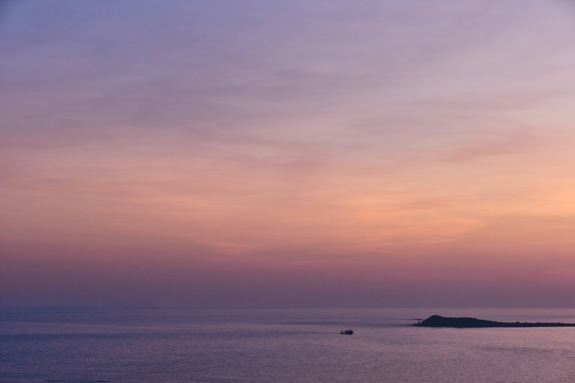 a sunset over a body of water with a small island in the distance