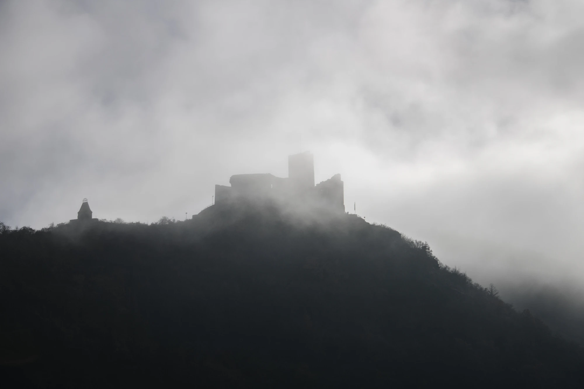 A solitary castle rising above a forested hill in thick morning fog