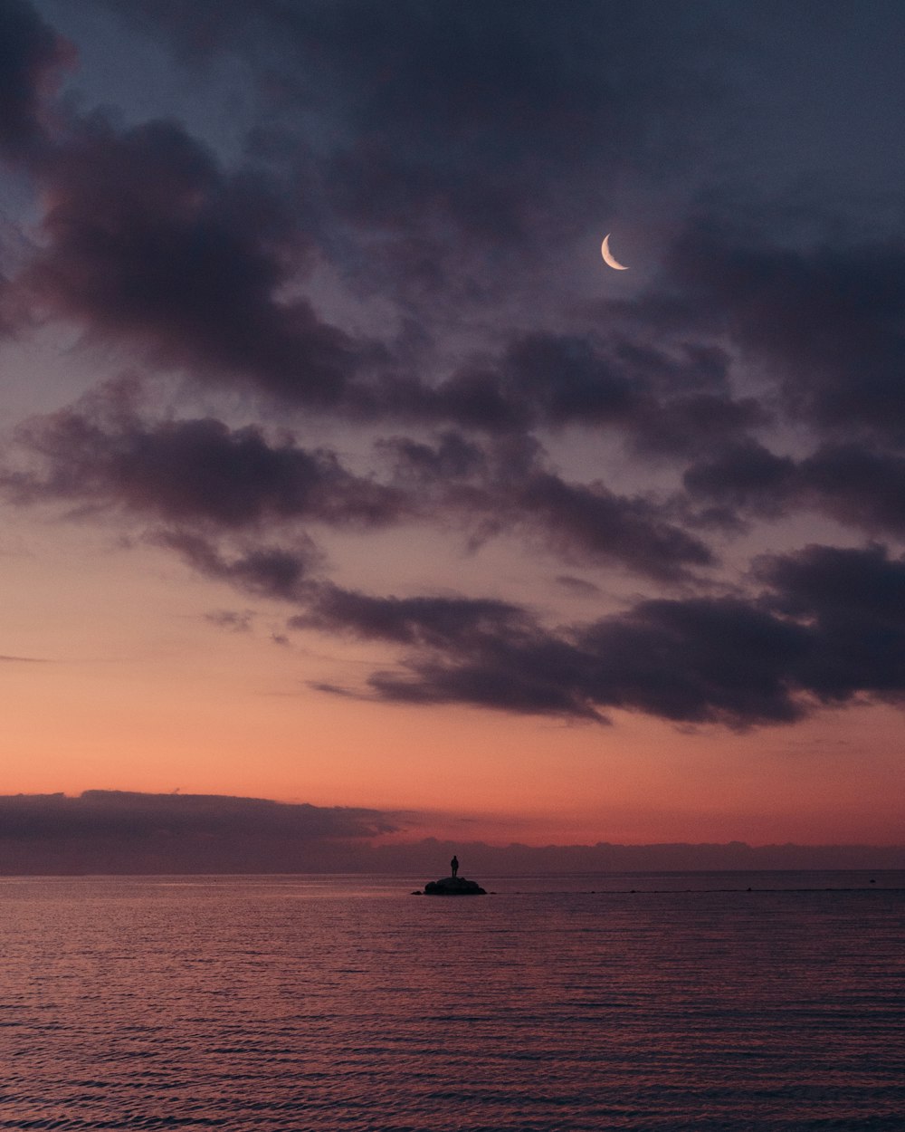 a boat in the ocean at sunset with a half moon in the sky