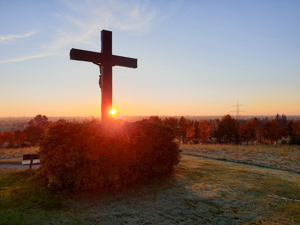 une croix sur une colline avec le soleil couchant en arrière-plan