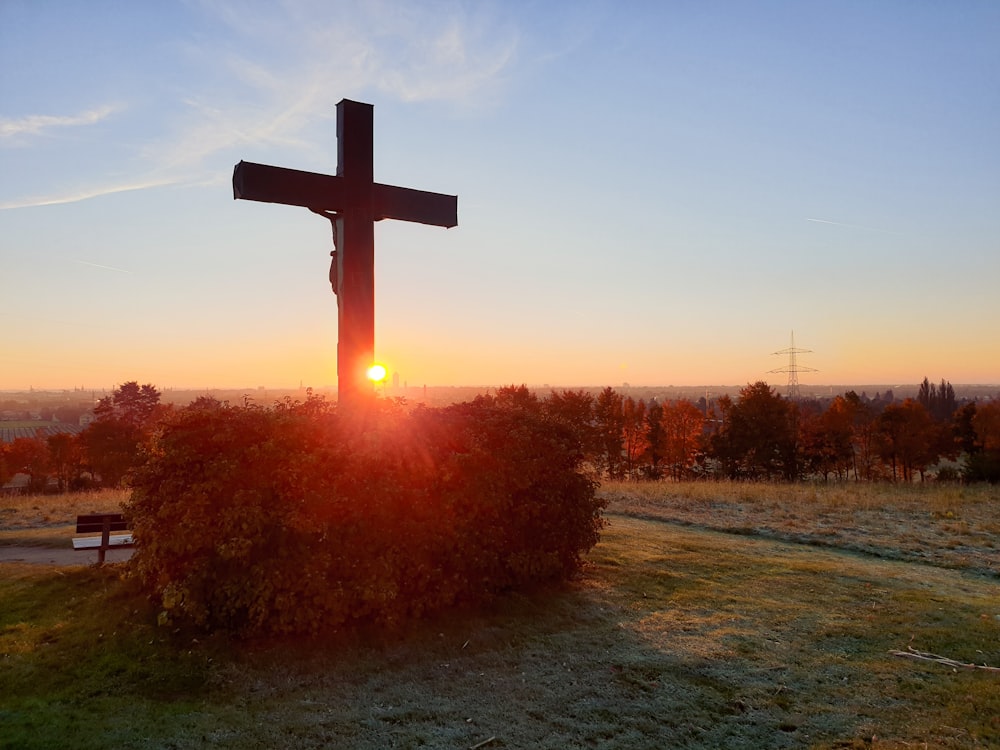a cross on a hill with the sun setting in the background