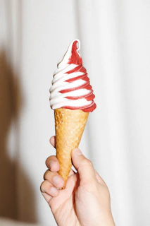 Close-up of creamy, swirled soft serve ice cream in a classic red and white striped cone holder.