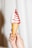 A hand is holding a soft serve ice cream cone swirled with red and white colors. The ice cream has a smooth texture, and the cone appears to be a waffle type. The background is a neutral, light color.
