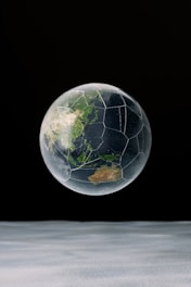 A spherical object resembling a globe is suspended against a dark background. The surface of the sphere features landmasses similar to a world map, though it's structured like a soccer ball with distinct hexagonal and pentagonal segments.