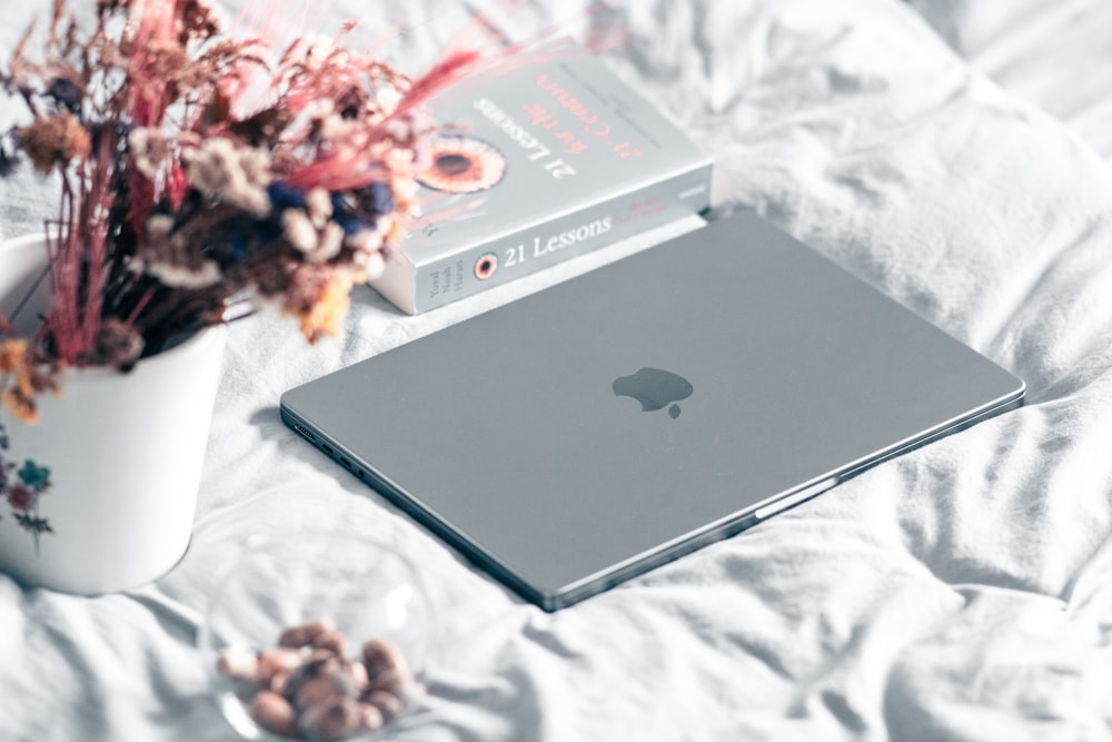 a laptop computer sitting on top of a bed next to a flower pot