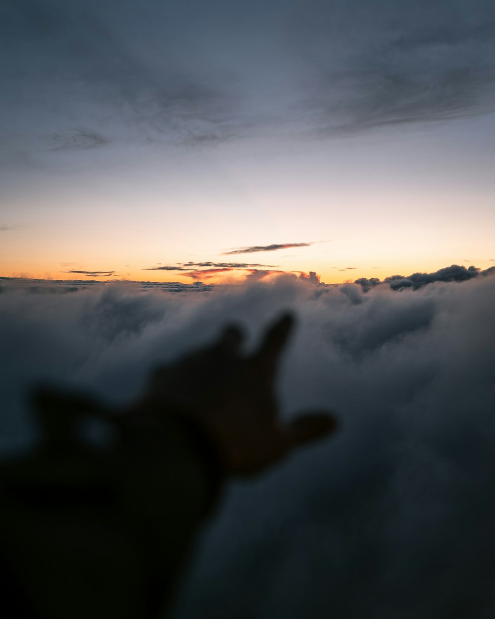 a person's hand reaching for the sky above the clouds