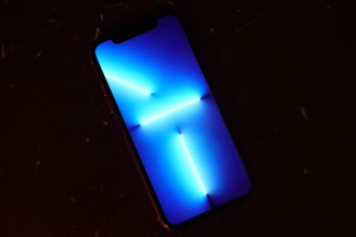 A smartphone displays a vibrant blue abstract pattern with sharp light streaks, set against a dark surface.