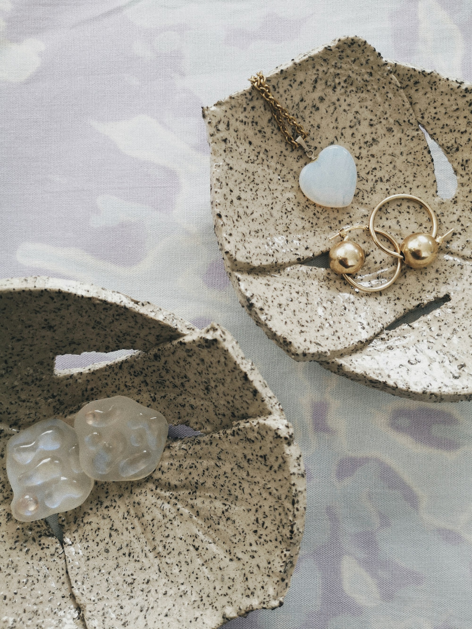 Moonstone heart necklace and gold earrings on monstera ceramic plate.