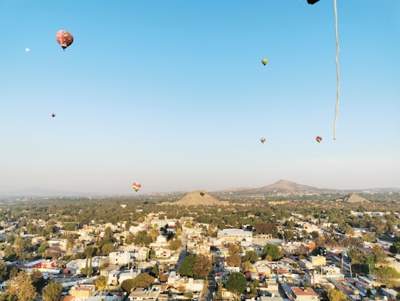 A colorful hot air balloon rising over the ancient pyramids of Teotihuacán at sunrise.