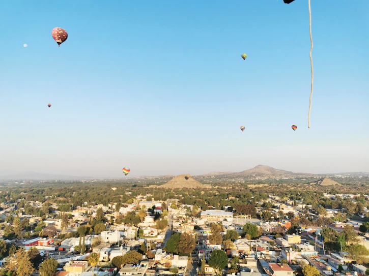 Hot air balloons soaring over the ancient pyramids of Teotihuacan at sunrise.