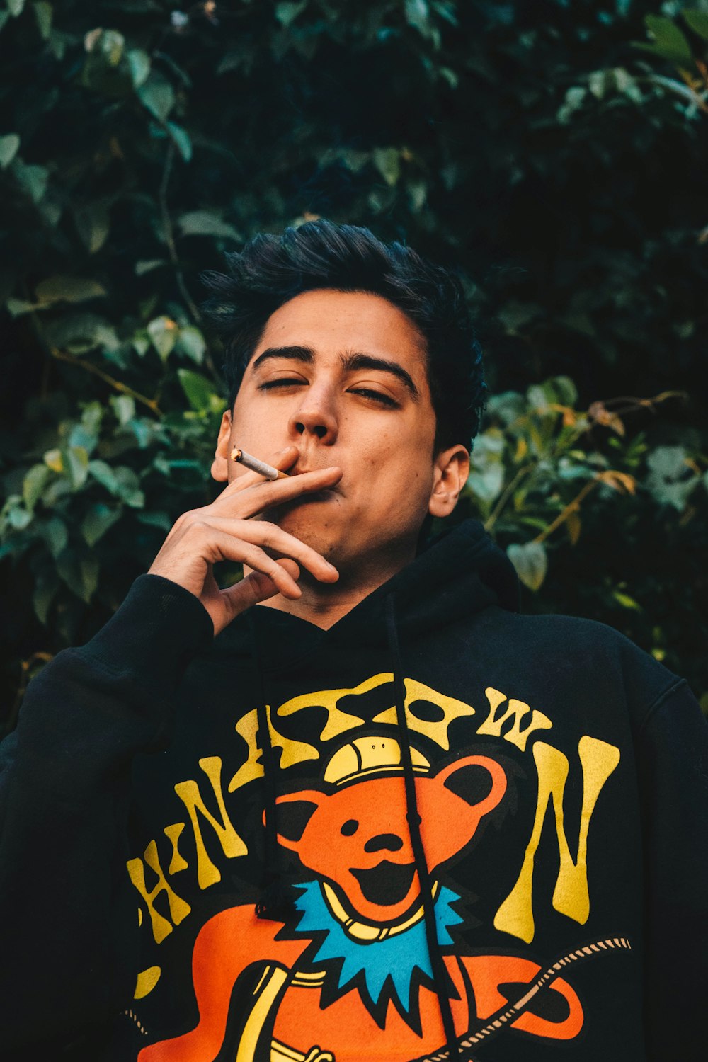 a man smoking a cigarette in front of a bush