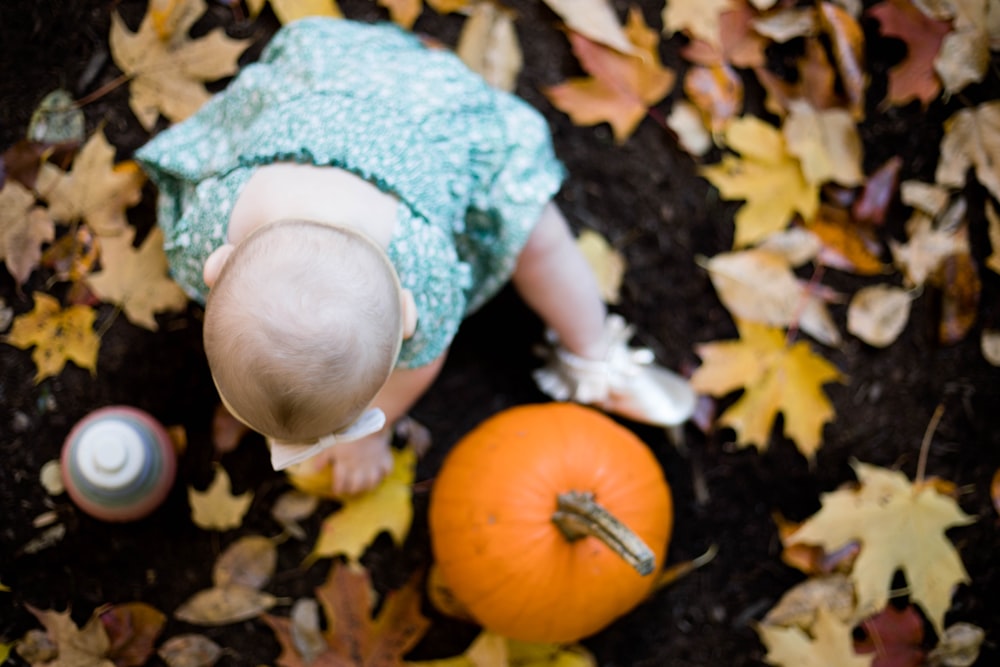 a baby in a blue dress playing with a pumpkin