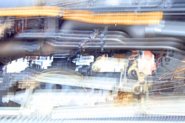 Blurred image of mechanical components with a mix of pipes, wires, and metal structures, likely part of machinery or an engine.