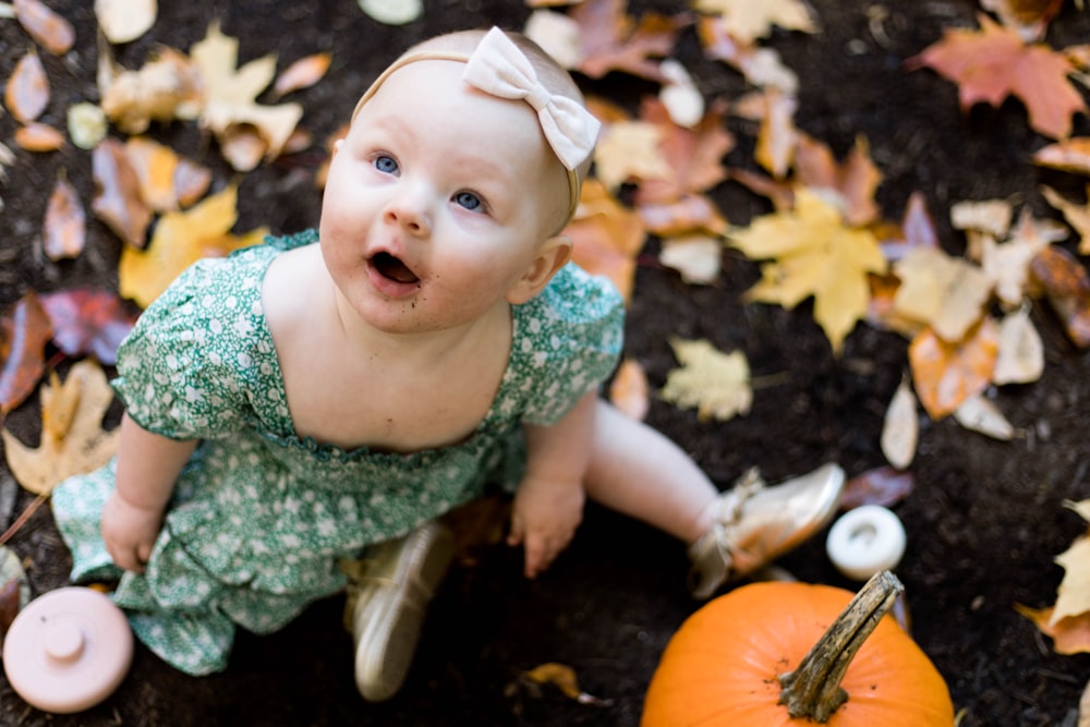 a baby sitting on the ground next to a pumpkin