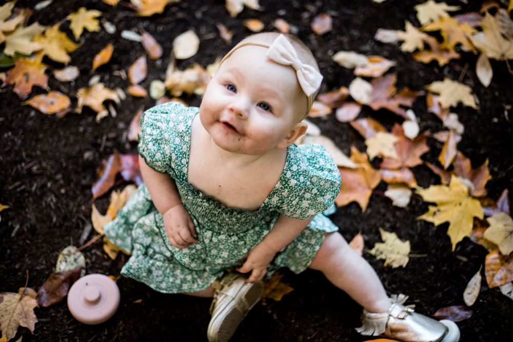 a baby girl sitting on a pile of leaves