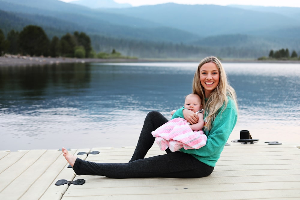 a woman sitting on a dock holding a baby