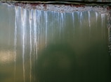 The image features a green metallic surface with noticeable streaks of rust and white corrosion lines descending vertically. The surface texture is rough, and the corroded areas display a contrast between the dark rust and the lighter spots.