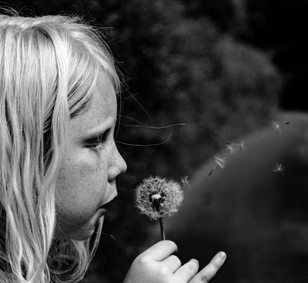 a girl blowing a dandelion with her hand