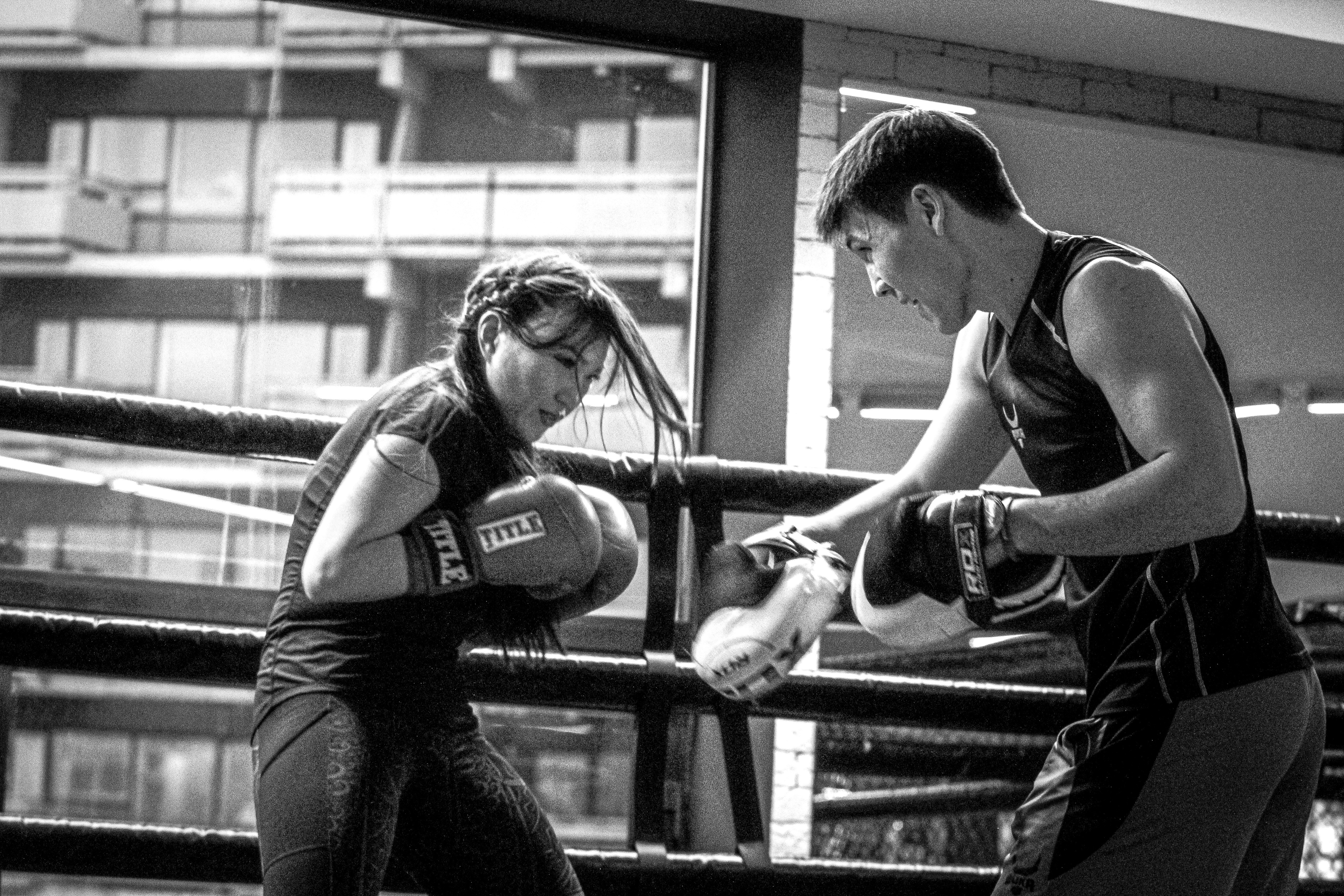 Female boxer sparring with a trainer in a gym, focusing intensely, embodying the strength and dedication of women's boxing workouts.