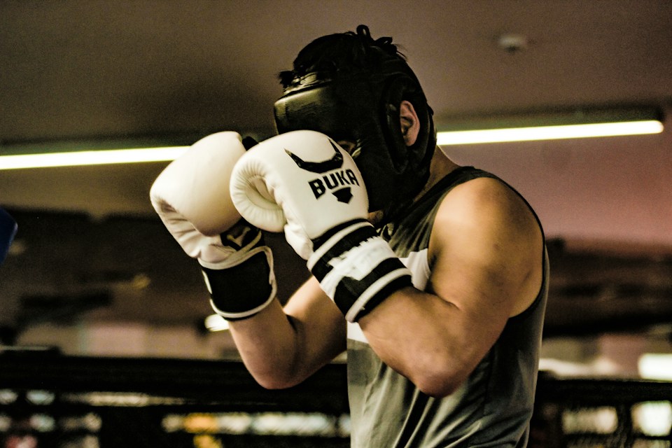 Boxer in headgear and white gloves holding a high guard during sparring practice