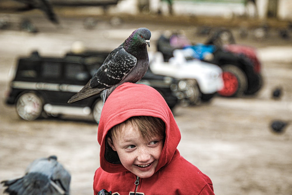 a boy in a red hoodie with a bird on his shoulders