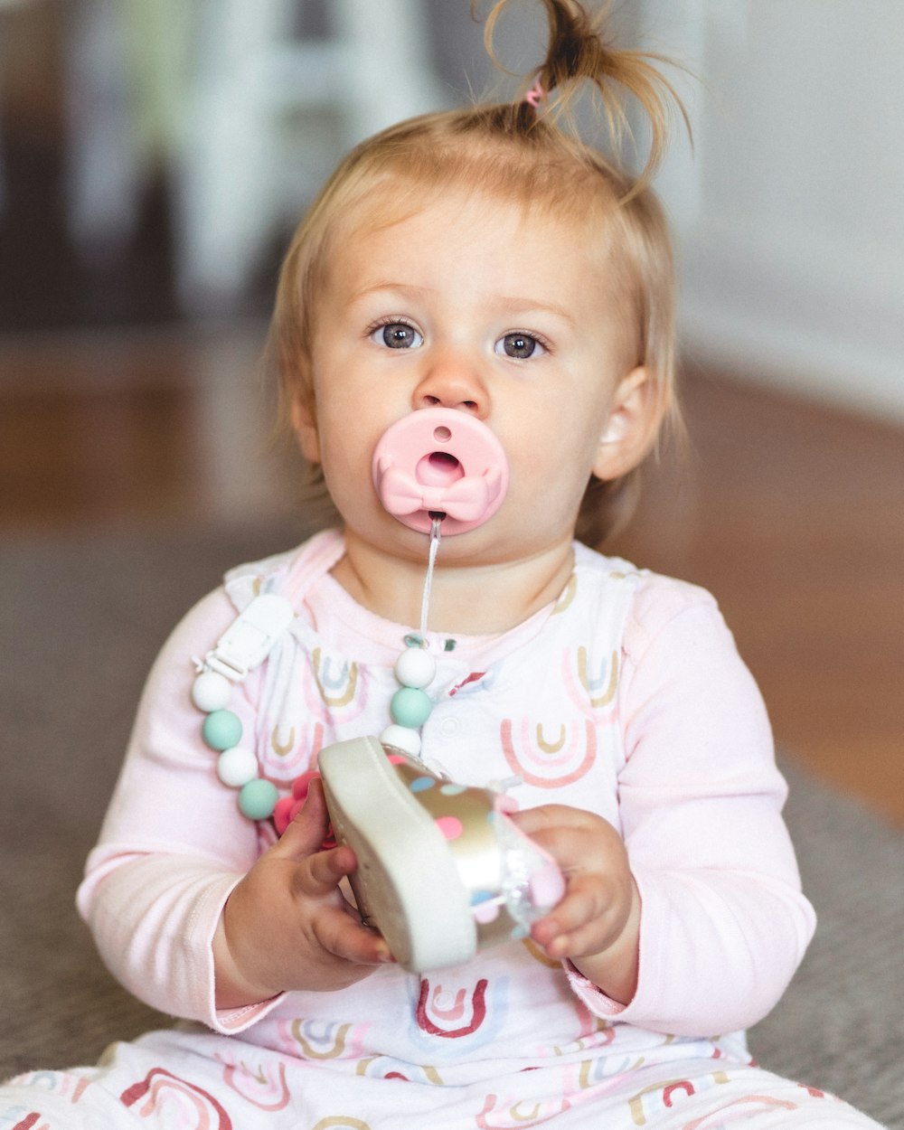 a little girl sitting on the floor with a pacifier in her mouth