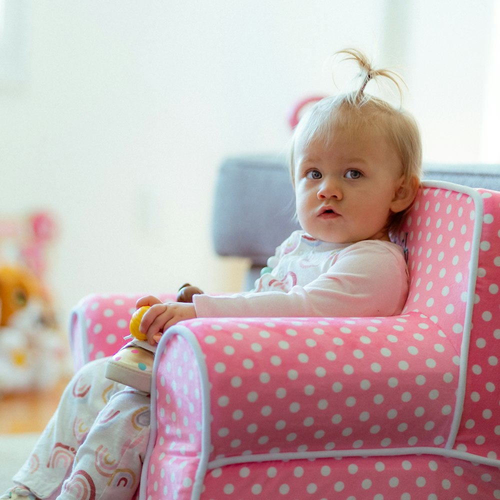 a little girl sitting in a pink chair