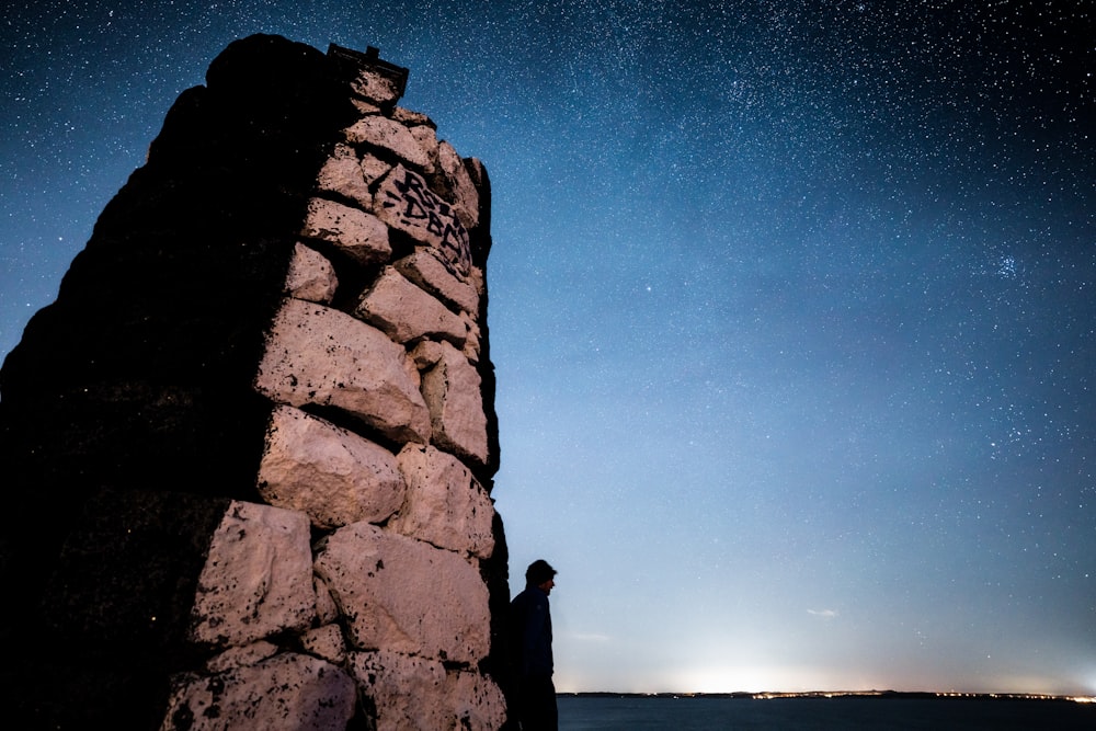 a person standing next to a rock wall under a night sky