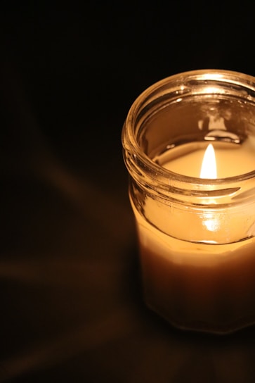 Warm, soft candlelight flickering inside a handcrafted jar against a soft beige backdrop.