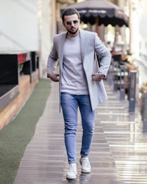 a man walking down a sidewalk wearing sunglasses