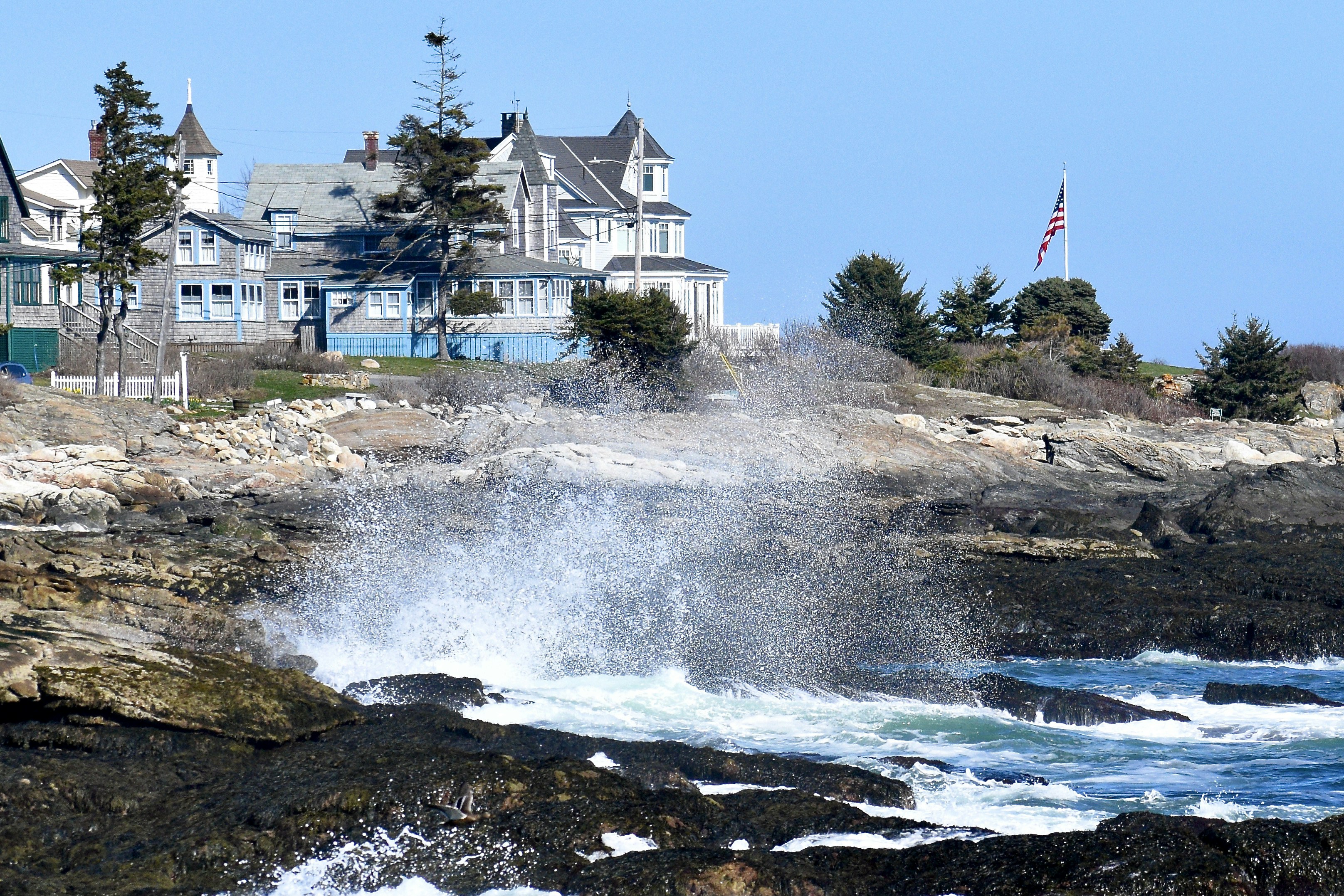 a large wave crashes into the rocks near a house
