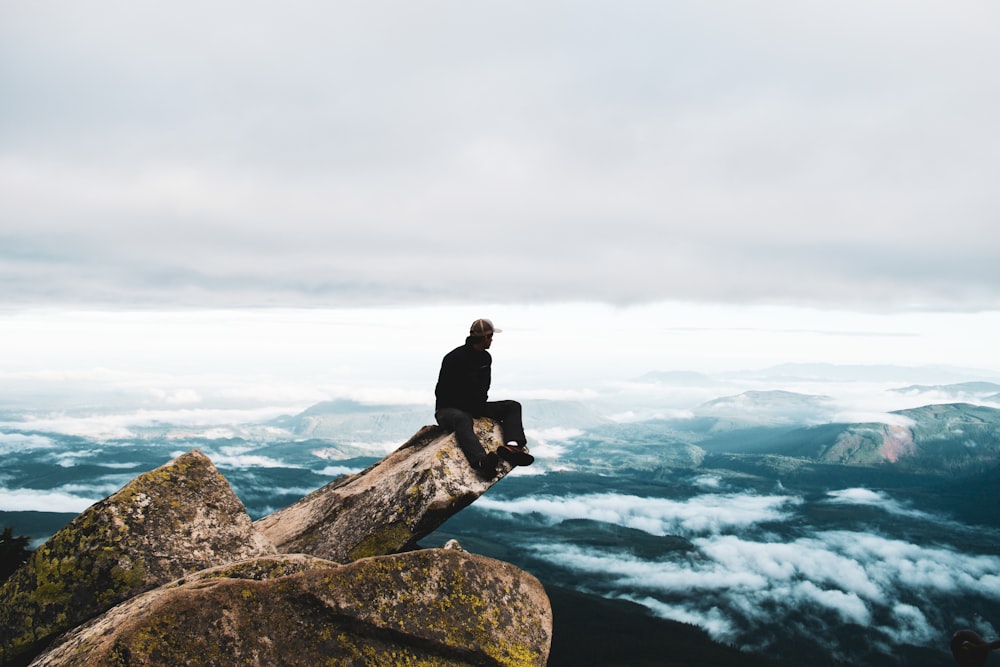 um homem sentado no topo de uma rocha no topo de uma montanha