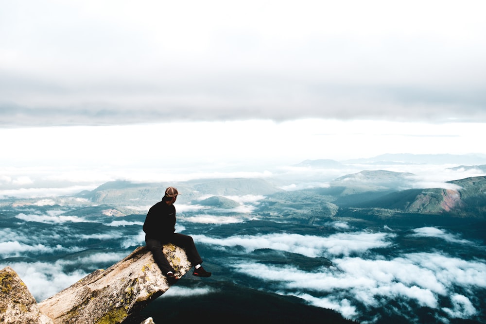 a man sitting on top of a cliff above the clouds